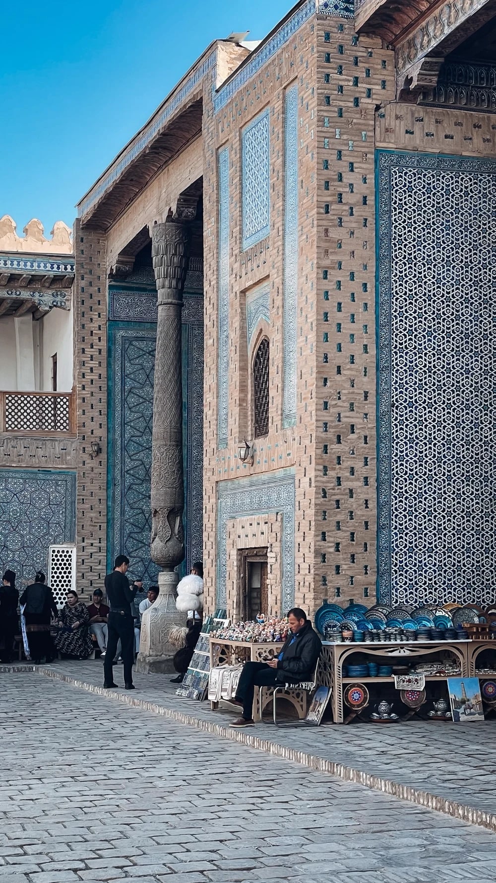 A ceramics vendor beside a carved column in Khiva